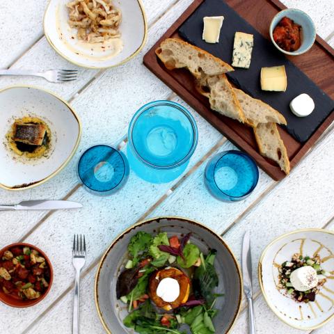 Gourmet Dining Table Setup With Variety Of Dishes Elegant dining table with cheese board, calamari, salad, bruschetta, pastry, and blue water.