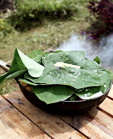Traditional Outdoor Cooking Pot With Green Leaves Black cooking pot covered with green leaves on a wooden surface outdoors