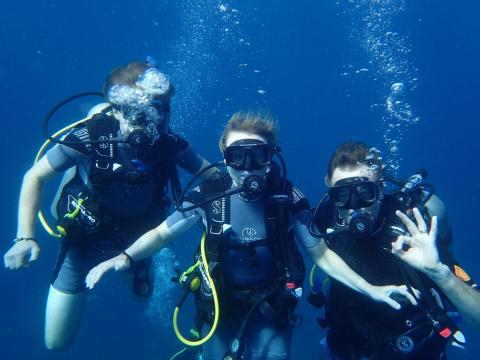 Scuba Divers Enjoying Underwater Exploration Three scuba divers in clear blue water making OK sign, happy underwater adventure.