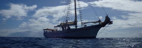 Sailing Ship Chronos On Open Ocean Adventure Blue-hulled sailing ship Chronos with furled sails on choppy ocean under partly cloudy sky