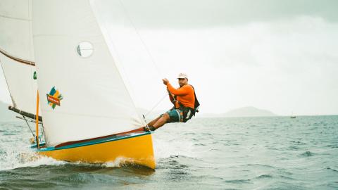 Man Sailing In Colorful Boat Near Coastline Man in orange shirt sailing on colorful boat near coastline