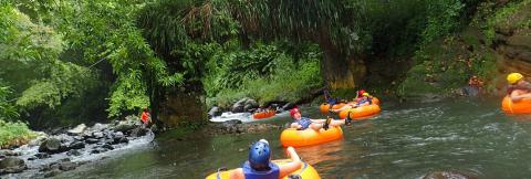 River Tubing Adventure In Lush Tropical Setting Group tubing on a calm river with orange tubes, helmets, and life jackets in lush scenery