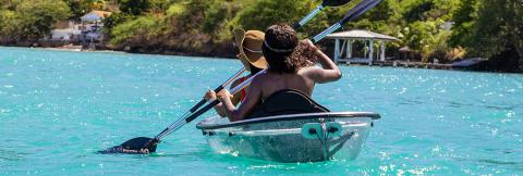 Kayaking In Clear Turquoise Sea With Lush Scenery Person kayaking in clear turquoise sea near lush greenery with a straw hat.