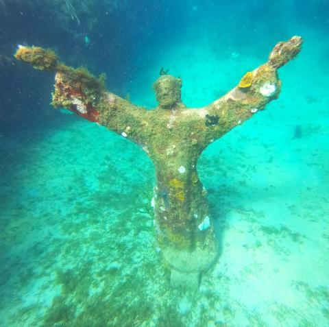 Underwater Statue Resembling Christ In Clear Shallows Underwater statue with marine life in clear shallow waters