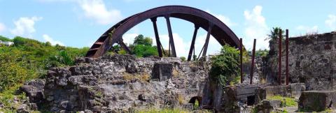 Old Industrial Sugar Mill Ruins With Rusty Wheel Ruins of an old industrial sugar mill with a large rusty wheel, near modern buildings.