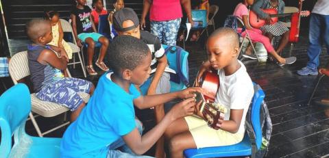 Kids Learning Guitar In Music Workshop Children in a music class learning to play guitar together.