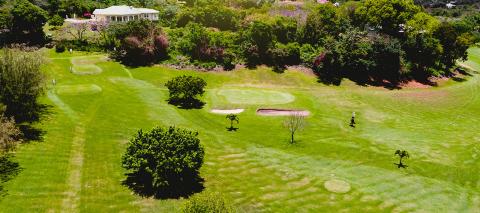 Aerial View Of Scenic Green Golf Course With Clubhouse Aerial view of a scenic golf course with lush greens, sand bunkers, and a clubhouse.