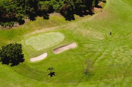 Aerial View Of Lush Golf Course With Players Aerial view of golf course with players, sand bunkers, and tree shadow