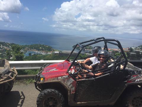 Adventure Atv Ride With Ocean View Two people in muddy ATV overlooking a scenic coastal bay on a sunny day