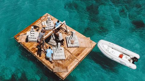 Team Building Wooden Raft On Clear Water Group building wooden raft with cinder blocks on clear deep water, motorboat nearby