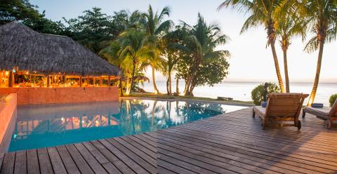 Luxury Tropical Resort Sunset With Infinity Pool Tropical resort with infinity pool, sea view, and thatched-roof bar at sunset