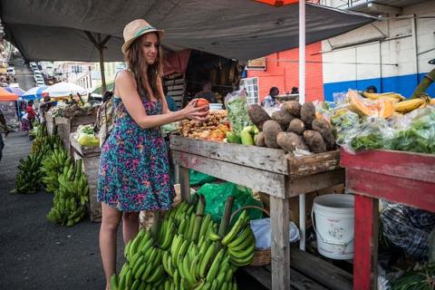 Woman Shopping For Fresh Produce At Outdoor Market Woman in straw hat examining red fruit at vibrant outdoor market.