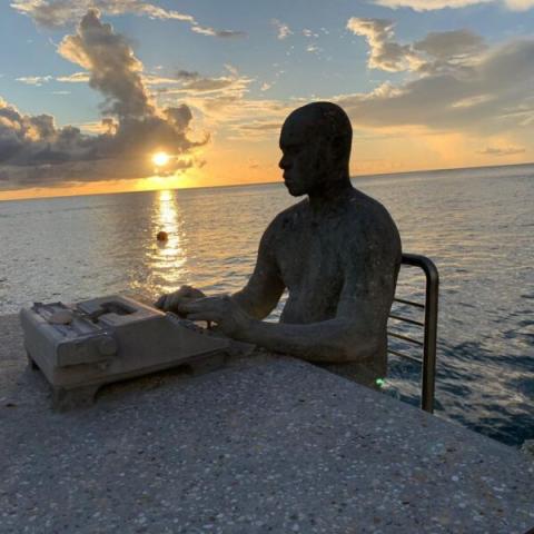 Statue Of Man Typing By Ocean At Sunset Statue of man on typewriter at sunset by ocean, artistic silhouette scene