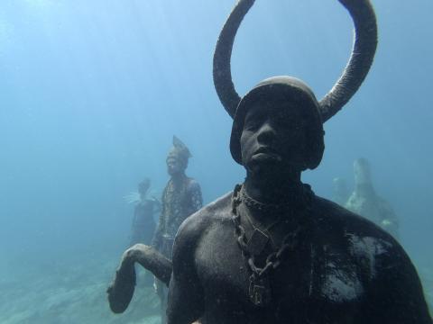 Underwater Sculpture Garden With Serene Horned Figure Underwater sculpture of person with horns in serene, artistic sea tableau.