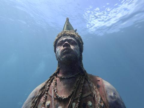 Underwater Sculpture Of Mythical Figure With Crown Underwater sculpture of a mythic figure with armor and crown in clear blue water.