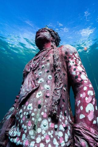 Underwater Statue Adorned With Corals And Barnacles Underwater statue of woman adorned with marine life in clear blue ocean