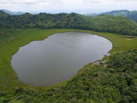 Aerial View Of Serene Lake And Lush Forest Aerial view of serene lake by forest with hills, structure, and vehicle
