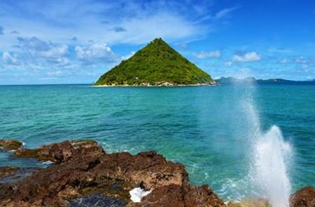 Scenic Lush Island View In Turquoise Sea Green island in turquoise sea with rocky shore and water splash under clear blue sky