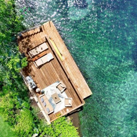 Turquoise Waterfront Deck With Daybed And Loungers Aerial view of a wooden pier with daybed and sun loungers by turquoise waters