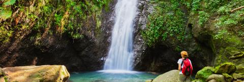 Serene Waterfall Hike With Person Enjoying Nature Person with red backpack admiring serene waterfall in lush landscape.