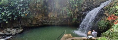 Serene Tropical Waterfall And Observers In Nature Tranquil waterfall and pool in a lush tropical setting with visitors enjoying the scene.