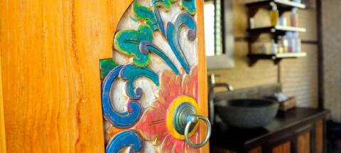 Carved wooden door with colorful patterns and metal handle in a rustic kitchen.