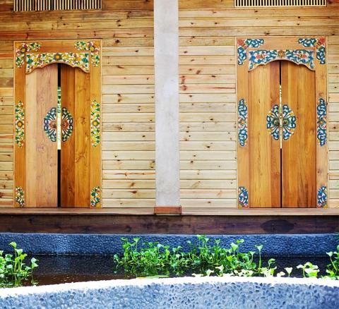 Traditional wooden doors with floral designs by a serene water feature in a garden setting.