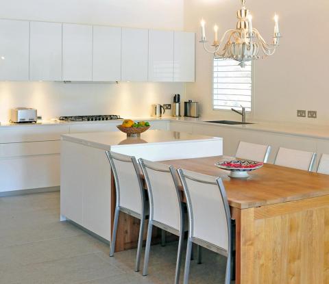 Minimalist white kitchen with wooden table, metallic chairs, and modern appliances.
