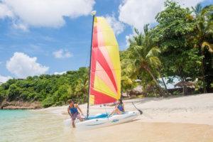Two people pulling a colorful catamaran on a tropical beach under clear skies