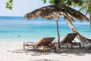 Serene beach scene with lounge chairs and thatched umbrella facing the sea.