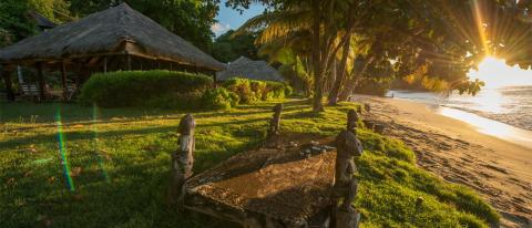 Sunrise at serene beach with palm trees, thatch-roof hut, and stone table.