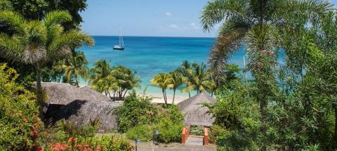 Tropical beach with palm trees, thatched hut, and sailboat on a calm blue sea