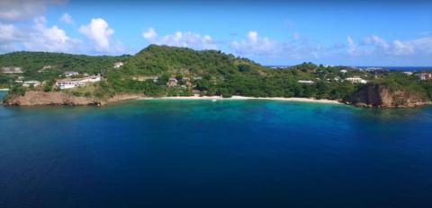 Panoramic tropical coastline with lush hills, blue sea, and white sandy beach.