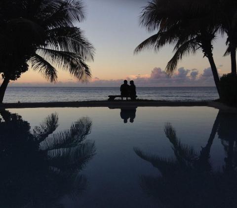 Sunset at beach with infinity pool, silhouetted figures and palm trees