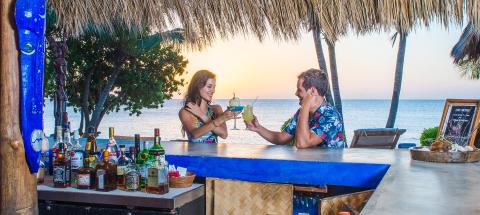 Man and woman enjoying cocktails at a sunset beach bar.