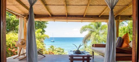 Luxurious outdoor living space overlooking ocean with lush greenery and sailboat.