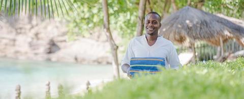 Smiling man with towel at tropical beach resort, white shirt with blue stripe