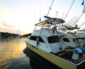 White and yellow sport fishing boat at sunset in marina with people on deck