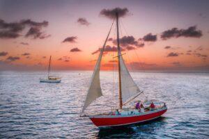 Red sailboat sailing on ocean at sunset with people on board