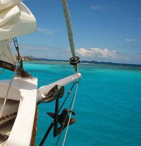 Boat bow with anchor overlooking clear turquoise sea and distant islands