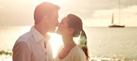 Couple near kissing at sunset on coast with sailboat background