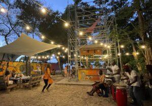 Outdoor community event at dusk with string lights, people, and a wooden stage.