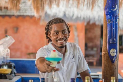 Cheerful bartender serves layered blue-green cocktail in tropical bar setting