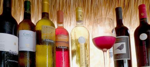 Row of chilled wine bottles with a glass of red wine against a rustic straw backdrop.