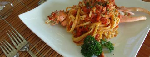 Delicious lobster spaghetti with tomato sauce and parsley garnish on a white plate.