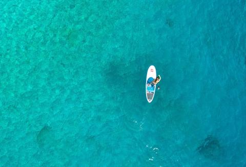 Paddleboarder in clear turquoise waters with visible sea features