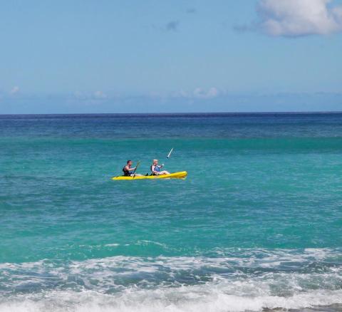Two people kayaking in a yellow kayak on a clear blue ocean under a sunny sky