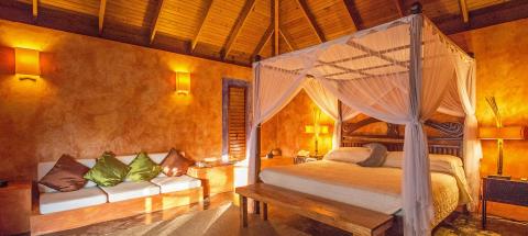 Cozy bedroom with wooden beamed ceiling, canopy bed, and modern sofa.
