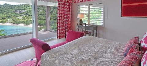 Modern bedroom interior with beach view, pink chairs, and red accents.