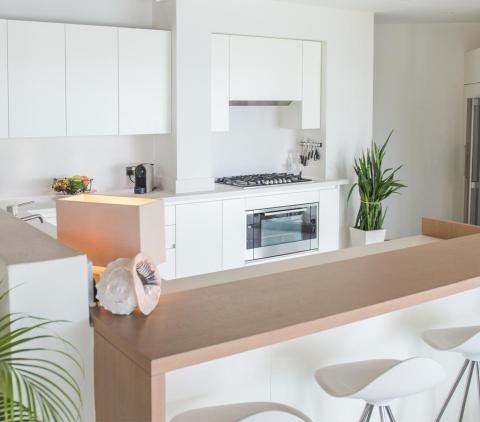 Modern minimalist kitchen with white cabinets, gas cooktop, and bar stools.